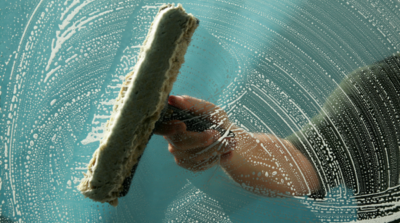 Picture through a soapy window of a hand washing it.