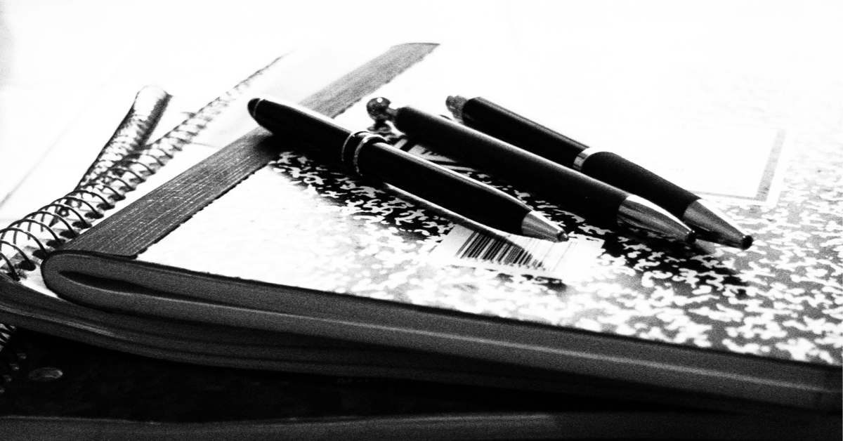 A black and white photo of three dark ballpoint pens lying diagonally on top of a mottled composition book on top of some other books. Image credit: Three Pens on a Composition Book (https://flic.kr/p/oEFEGs) by Leslie Richards, licensed CC BY (https://creativecommons.org/licenses/by/2.0/).